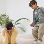 Boy jumping on the sofa next to his mother